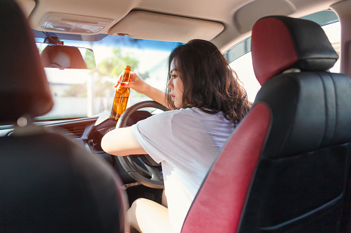 Young asian woman drinking beer while driving a car.
