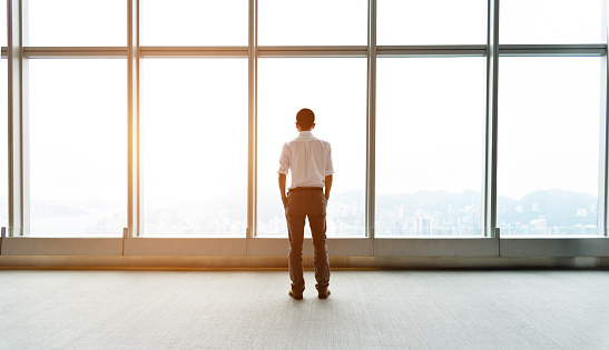 Businessman standing looking out of the window in a modern business building.