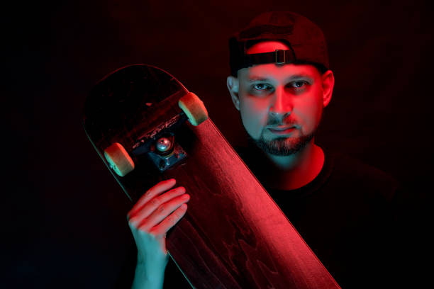 istock Skateboarder in black shirt with skateboard on neon light background 1156868660