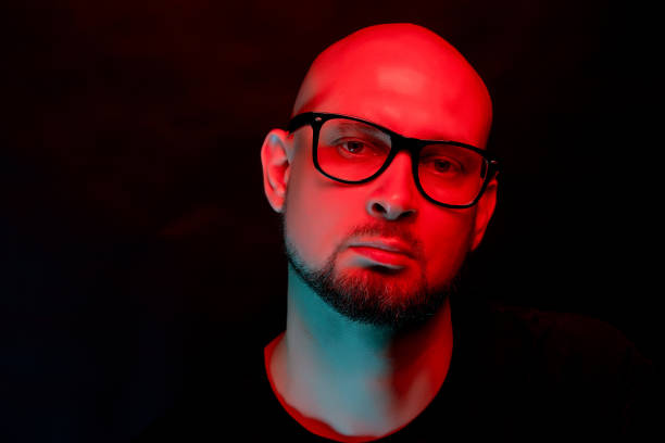 istock Attractive bald man with beard in glasses on neon light background 1156869212