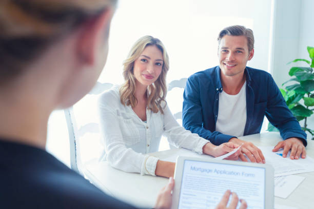 istock Real estate agent with couple looking through documents. 1156869859