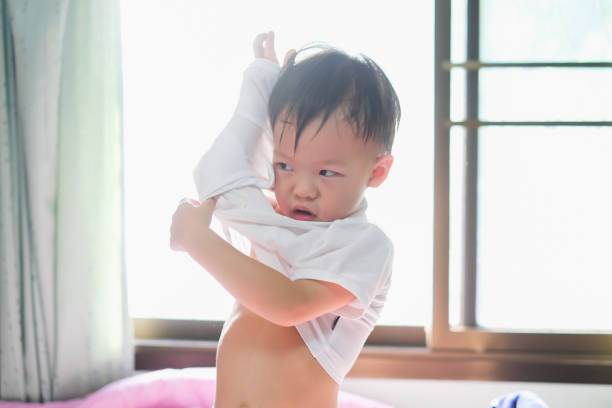 Asian 2 - 3 years old toddler boy child in bed concentrate on putting on his shirt, Encourage Self-Help Skills in Children stock photo