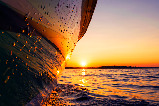 Side view Speeding fishing motor boat with drops of water. Blue ocean sea water wave reflections at the sunset. Motor boat in the blue ocean. Ocean yacht. Sunset at the sailboat deck