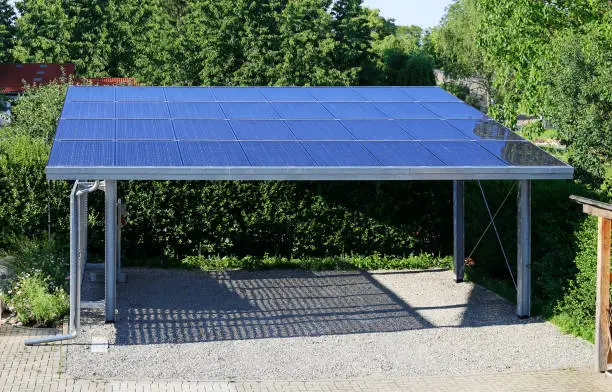 Modern semi-transparent photovoltaic modules made of glass replace the roof of a carport. Very long life with high efficiency and translucent material is the future for renewable energy. Own electricity for electric cars makes sense.