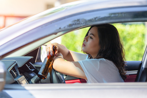 Young asian woman drinking beer while driving a car