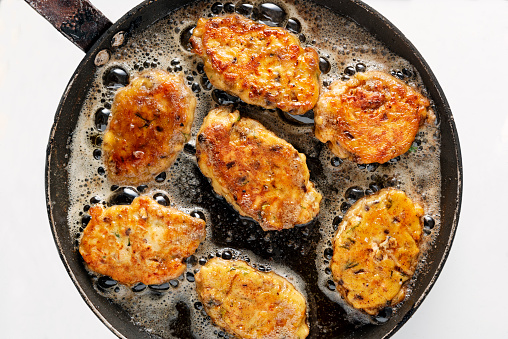 Traditional Danish Fiskefrikadeller or fish cakes, frying in a pan. Fiskefrikadeller are made from finely chopped white fish, usually cod  or haddock, with small pieces of more roughly chopped salmon added, along with cream, onion, carrot and  flour, salt and white pepper. Served with slices of lemon and remoulade. Colour, horizontal with some copy space.