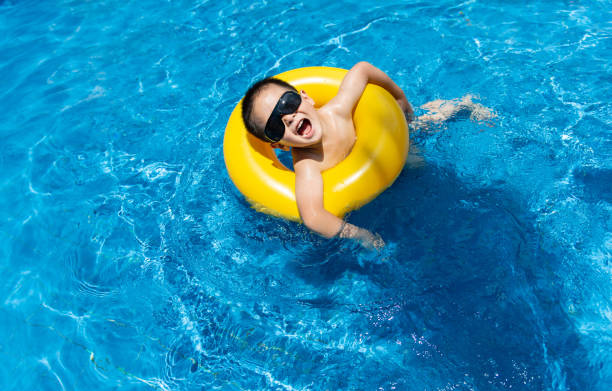 Happy Asian boy with swim ring floating on surface blue water. Relaxing kid playing with inflatable ring in outdoor swimming pool on summer holiday vacation. Joyful child swimming in pool on weekend.