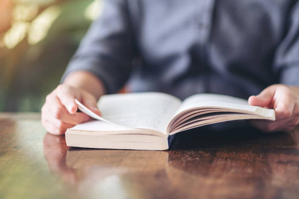 istock a woman holding and reading a vintage novel book 1156876152
