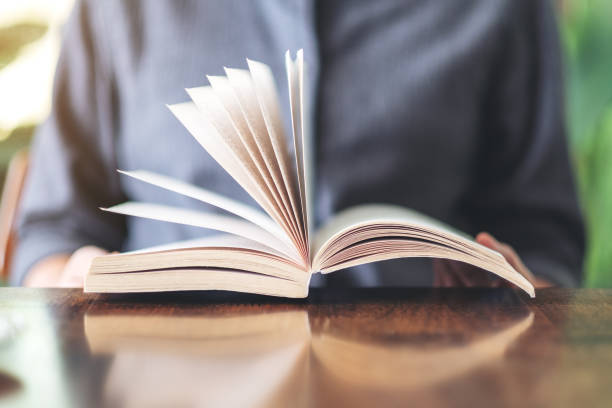 istock a woman holding and reading a vintage novel book 1156876187