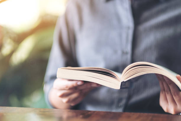 istock a woman holding and reading a vintage novel book 1156876199