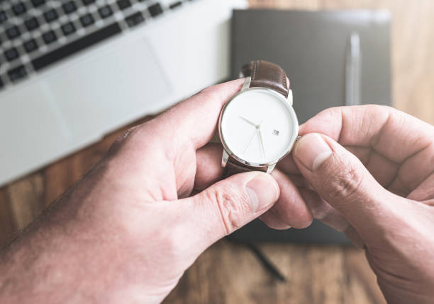 homem que estabelece seu relógio de pulso contra o computador portátil e organizador pessoal na mesa - instrumento para medir o tempo - fotografias e filmes do acervo