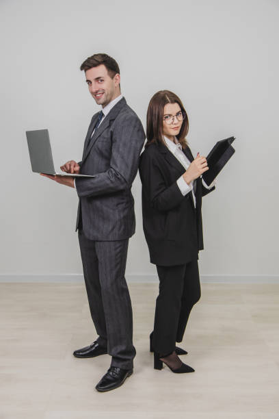 istock Full-length busy successful work partners standing shoulder to shoulder, checking data, looking pleasantly at the camera. Man working with laptop, woman with tablet. 1156885897