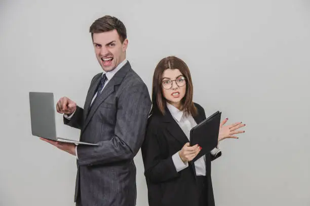 Photo of Busy successful work partners standing shoulder to shoulder, checking data. Man working with laptop, looking with irritated face expression, woman with tablet, setting her teeth.