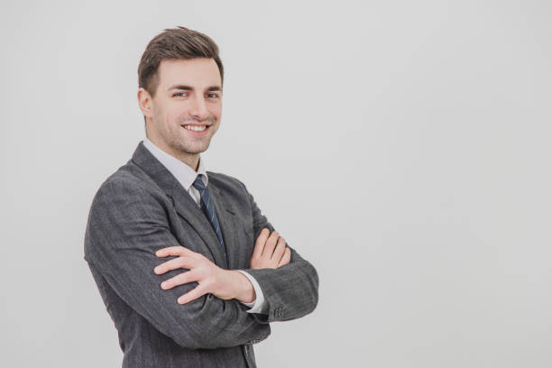 istock Serious handsome businessman standing camera right, smiling, his hands folded. 1156886020