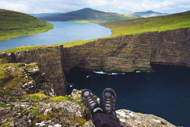 Legs of hiker sitting on top of a cliff over lake Sorvagsvatn on Faroe Islands Legs of hiker sitting on top of a cliff with views over cliff Traelanipan and lake Sorvagsvatn located on the island of Vagar in the Faroe Islands, Denmark. vágar photos stock pictures, royalty-free photos & images