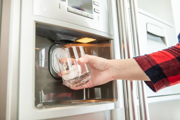 Woman's hand holds glass and uses refrigerator to make fresh clean ice cubes. stock photo