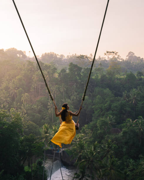Young happy woman enjoying in her day at nature. Rear view of a Women sitting on swings at a height of more than twenty meters. In Indonesia Bali Province. Photo of Young tourist woman swinging on the cliff in the jungle rainforest of a tropical Bali island. Young woman swinging in the jungle rainforest of Bali island, Indonesia. Swing in the tropics. bali stock pictures, royalty-free photos & images