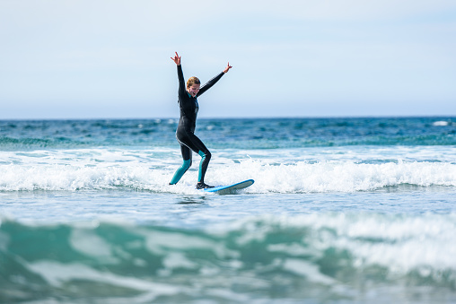 Surfer girl surfing with surfboard on waves in Atlantic ocean. Woman in surfing wet suit is active surfing the waves of cold atlantic ocean in Galicia, Spain.