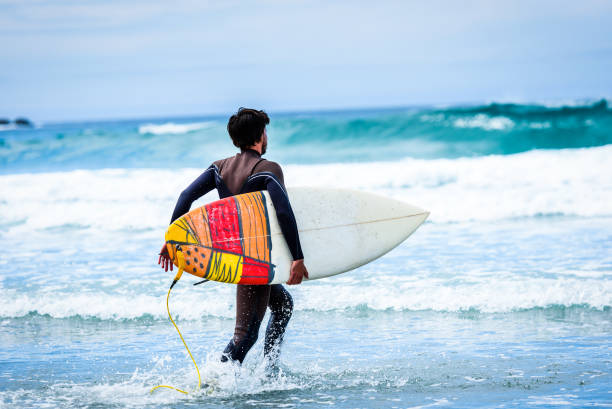 istock Surfer guy with surfboard in hand running towards big waves. 1156893310