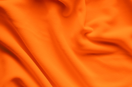 Background texture of bright orange fleece, soft napped insulating fabric made of polyester, wavy pattern, top view