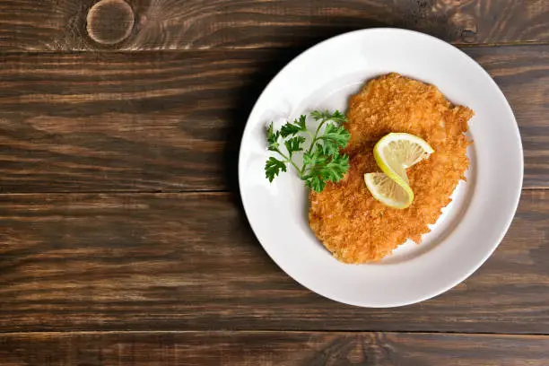 Chicken schnitzel on plate over wooden background with copy space. Top view, flat lay