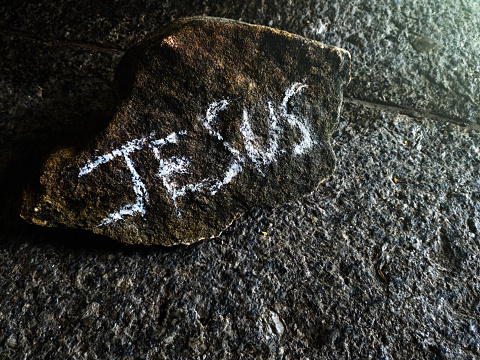 Someone has written Jesus on a piece of rock and left it lying on a paving stone.