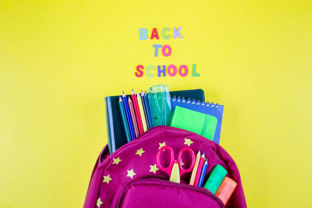 istock Red backpack with different colorful stationery on yellow background. Back to school concept. Top view, copy space 1156904553