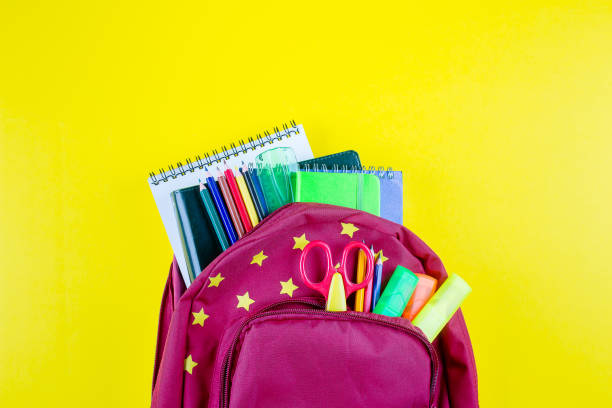 istock Red backpack with different colorful stationery on yellow background. Back to school concept. Top view, copy space 1156904622