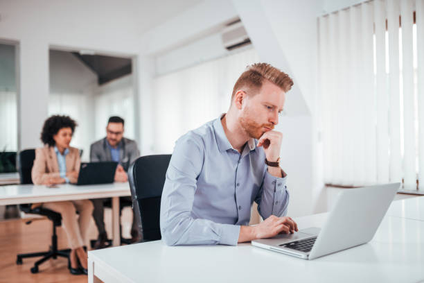 istock Puzzled redhead businessman looking at laptop screen in co working office. 1156908965