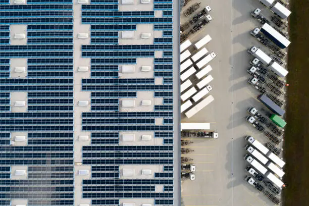 Aerial view of semi trucks during unloading and a large storehouse with solar panels on the rooftop.