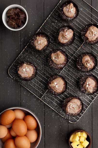 istock Fairy cakes on a cooling tray with  a dusting of icing sugar and ingredients, on a distressed grey wooden background 1156913986