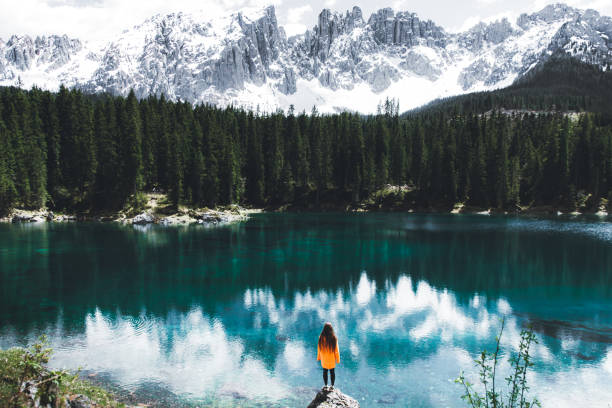 femme dans l'imperméable restant sur le rocher et regardant lago di carezza dans les alpes de dolomites - european alps mountain mountain peak rock photos et images de collection