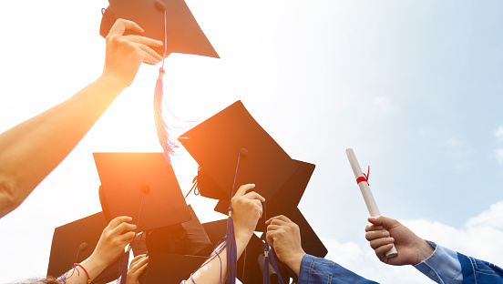 Group of graduate students throwing graduation hats to the sky.