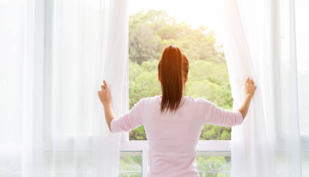 giovane donna asiatica che apre le tende e guarda fuori dalla finestra - curtain window women opening foto e immagini stock