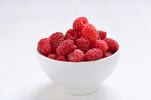 Raspberries in white bowl on table, close up view