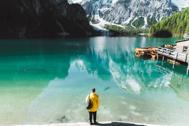 istock Man with backpack in raincoat looking at Lago Di Braies during summer sunrise 1156921719