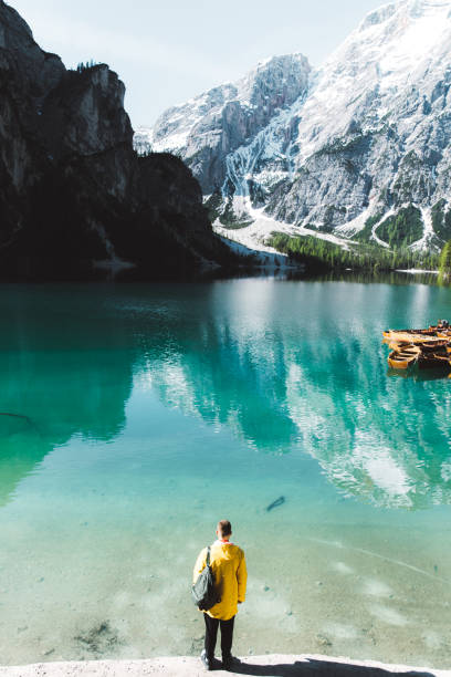 istock Man with backpack in raincoat looking at Lago Di Braies during summer sunrise 1156921881