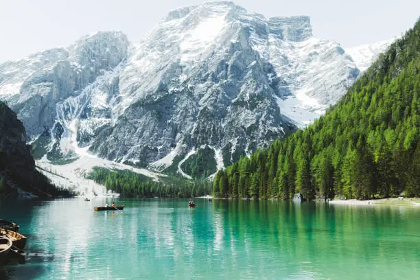 View of turquoise mountain lake, snowcapped mountains, pine forest and orange boats in South Tyrol - Italy