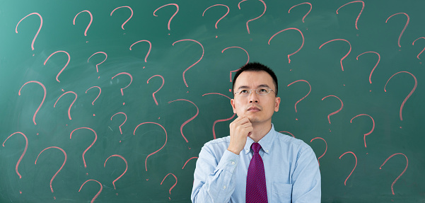 Asian businessman in front of blackboard with question marks.