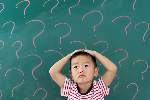 Asian little boy in front of blackboard with question marks.