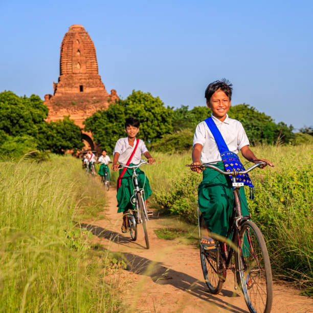 Burmese school children riding a bicycle in Bagan, Myanmar Young Burmese school children riding a bicycle, the ancient temples of Bagan on the background, Myanmar (Burma) bagan archaeological zone stock pictures, royalty-free photos & images