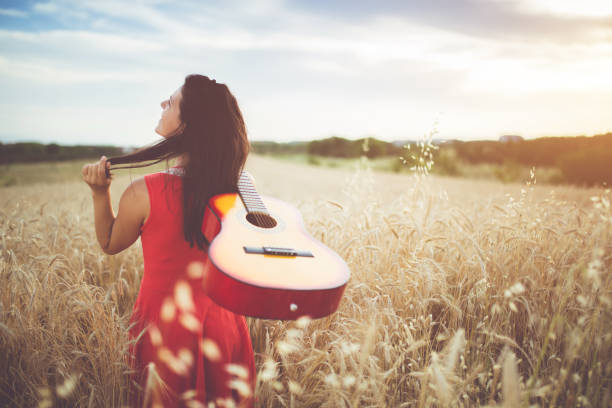 istock Woman walking through the wheat field with guitar on back 1156930847
