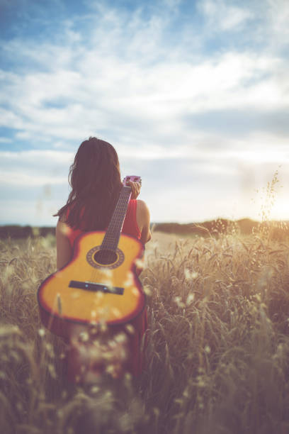 istock Woman walking through the wheat field with guitar on back 1156930877