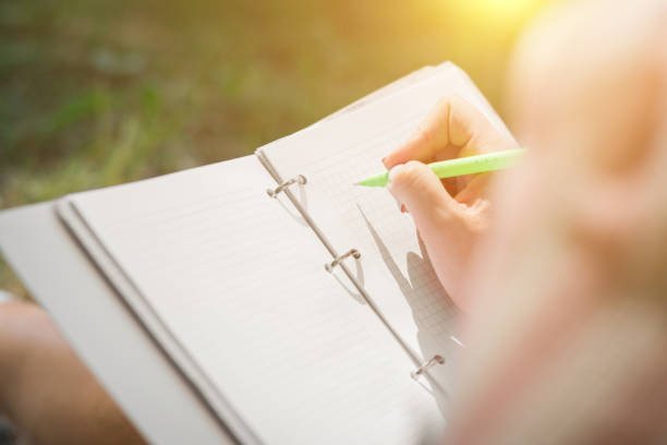 girls hands with pen writing on notebook in urban park summer day