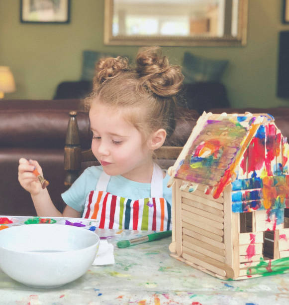 Crafting A happy little girl is painting a house built from popsicle sticks. popsicle stick stock pictures, royalty-free photos & images