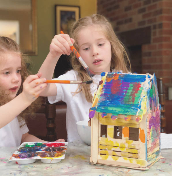 Crafting Two little girls are painting a house built from popsicle sticks. kids play house stock pictures, royalty-free photos & images