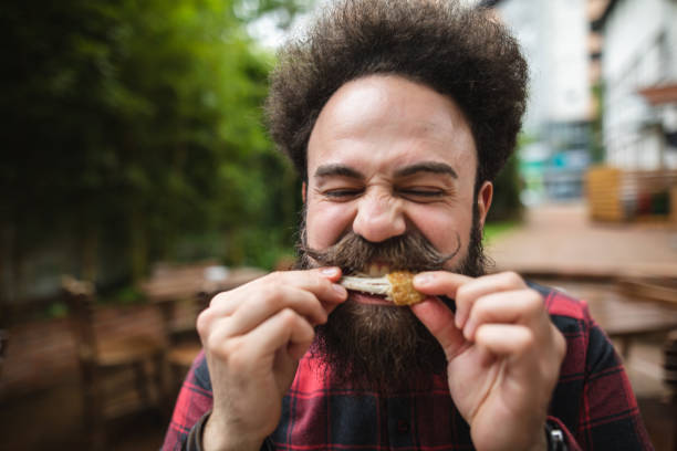 istock Bearded hipster with a pointy mustache eating a chicken wing 1156940538