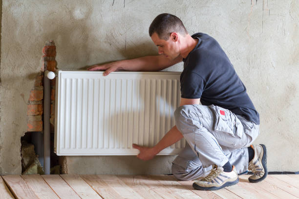istock Young handsome professional plumber worker installing heating radiator in an empty room of a newly built apartment or house. Construction, maintenance and repair concept. 1156942403