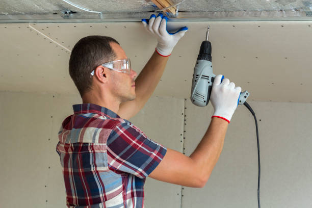 istock Young man in goggles fixing drywall suspended ceiling to metal frame using electrical screwdriver on ceiling insulated with shiny aluminum foil. Renovation, construction, do it yourself concept. 1156942513