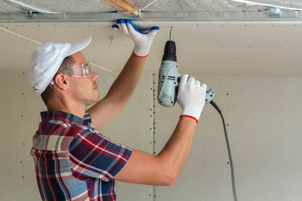 istock Young man in goggles fixing drywall suspended ceiling to metal frame using electrical screwdriver on ceiling insulated with shiny aluminum foil. Renovation, construction, do it yourself concept. 1156942530